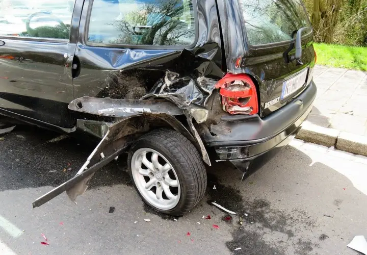 Czarny samochód po kolizji, z widocznymi uszkodzeniami tylnej części i koła.
