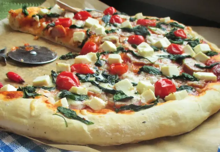 Pyszna pizza ze szpinakiem, pomidorkami koktajlowymi i kostkami sera feta. Idealna na szybki obiad.