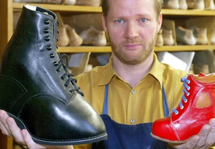 Schuhmacher hält einen schwarzen und einen roten Schuh, die für Klumpfuß-Kinder gefertigt wurden.