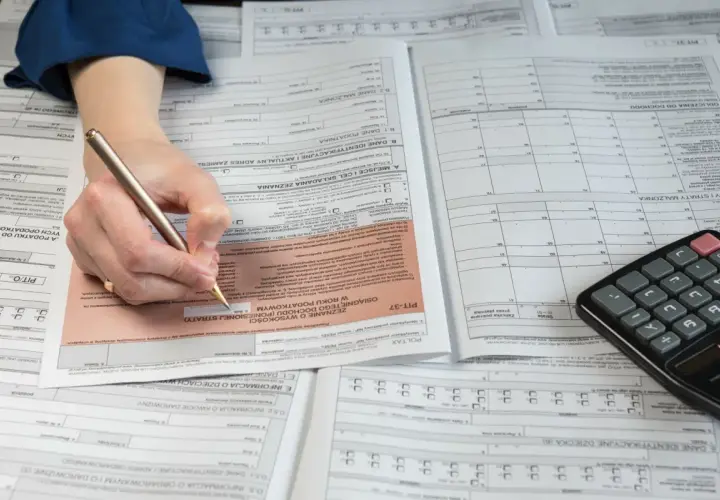 Ręka z długopisem wypełnia formularz PIT-37, obok leży kalkulator. To pomoc w rozliczeniu PIT 36.