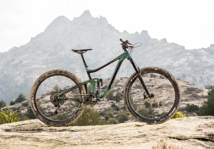 A 2020 Giant Reign mountain bike rests on a rocky outcrop, ready to conquer the rugged, misty mountains in the background.