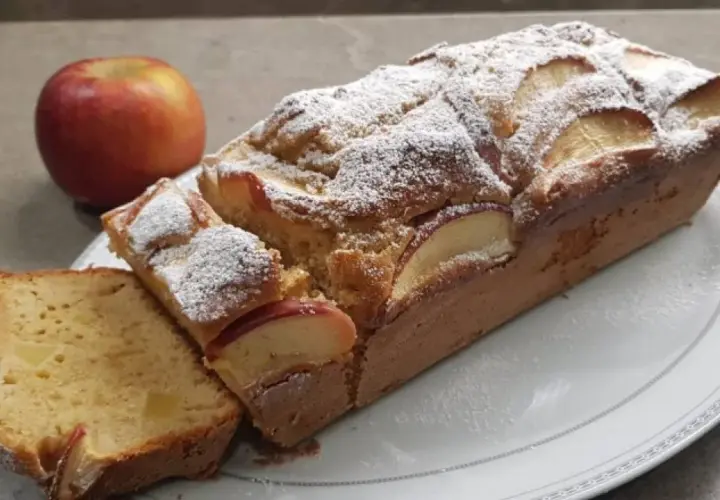Plumcake alle mele soffice e profumato, cosparso di zucchero a velo, con fette di mela a vista. Una mela rossa intera sullo sfondo.