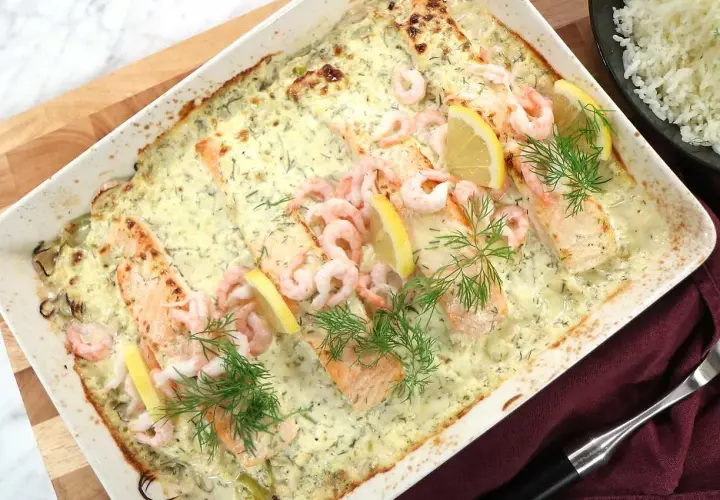 Lax med apelsinsås, toppad med räkor och citronklyftor, serveras i en ugnsform. Dillkvistar ger en fräsch touch.