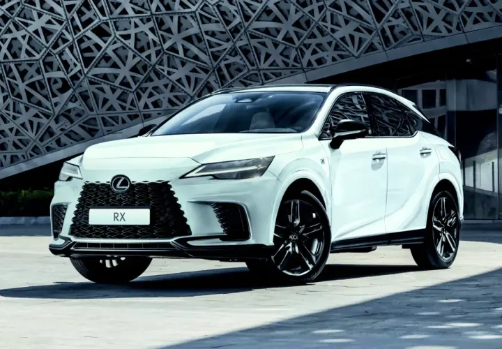 Biały Lexus RX 500h z czarnymi felgami stoi przed nowoczesnym budynkiem o geometrycznej fasadzie.