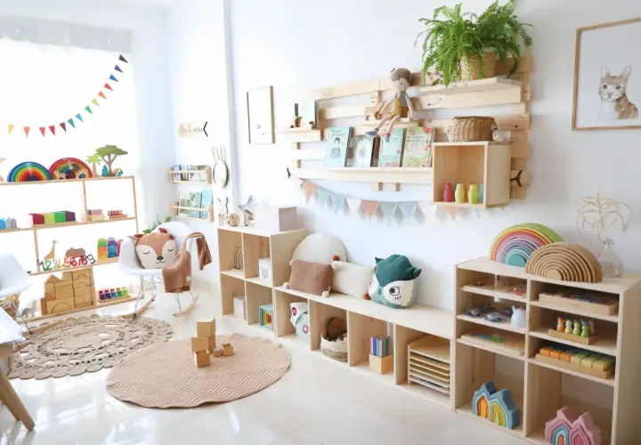 Un rincón Montessori lleno de juguetes de madera, arcoíris y peluches. Estanterías de pino organizan libros y materiales educativos.