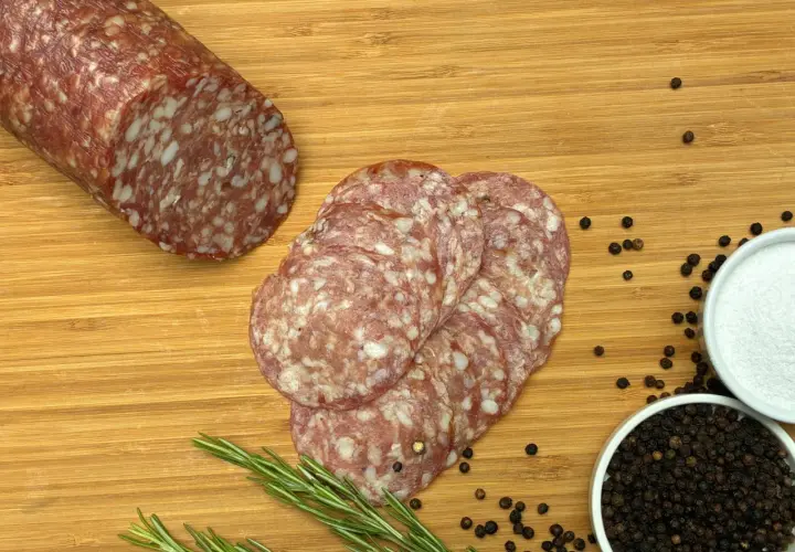Kawałek salami napoli i kilka plastrów na desce z rozmarynem, pieprzem i solą.