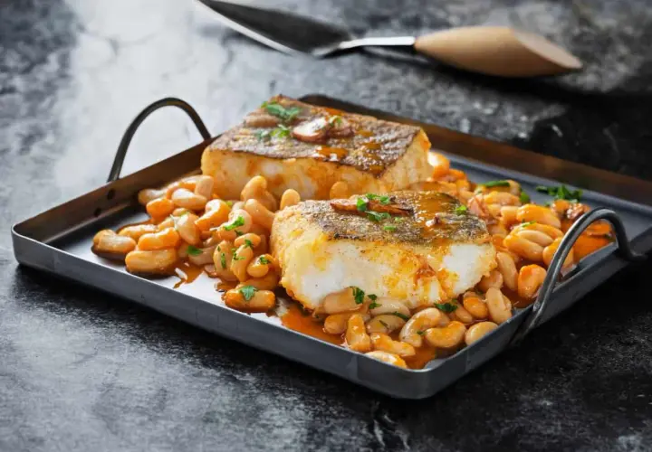 Dos lomos de bacalao a la llauna, dorados y jugosos, reposan sobre una cama de alubias blancas en salsa.