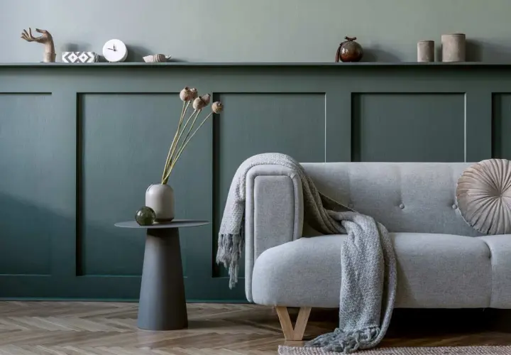 Soggiorno con divano grigio, coperta e decorazioni su una parete con effetto boiserie con pittura verde petrolio.