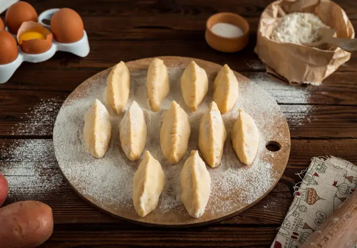 Gotowe do lepienia pierogi na desce, obok jajka i mąka. Czy ciasto na pierogi można zamrozić? Tak, to świetny sposób na zapas!