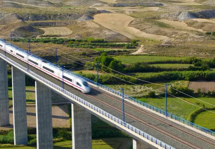 Un tren de alta velocidad cruza un viaducto sobre un paisaje rural. El tren, que parece ir de Lleida a Madrid, es plateado con una franja morada.