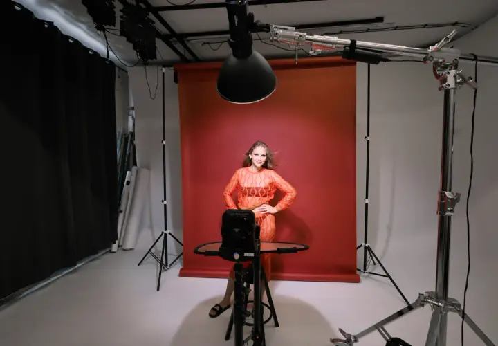 Modelka w studiu, testująca różne rodzaje oświetlenia w fotografii. Czerwone tło, lampy studyjne i sprzęt do tworzenia efektów.