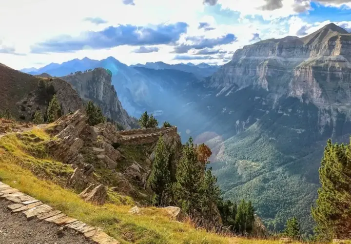Sendero de piedra serpentea por la ladera con vistas a un profundo valle en los Pirineos de Huesca.