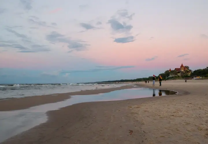 Zachód słońca nad morzem w Łebie. Spacer po plaży, w oddali widać budynek przypominający zamek. Idealne miejsce, by zobaczyć, co zwiedzić w Łebie.