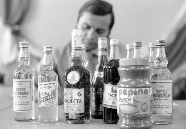 Mężczyzna bada butelki z alkoholem, w tym wódkę i brandy. Proces kupażowania może prowadzić do mętnienia wódki po dodaniu wody.