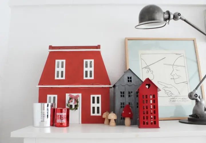 Un pueblo de casitas de navidad de madera, con una casa roja grande y otras más pequeñas, adornos y velas.