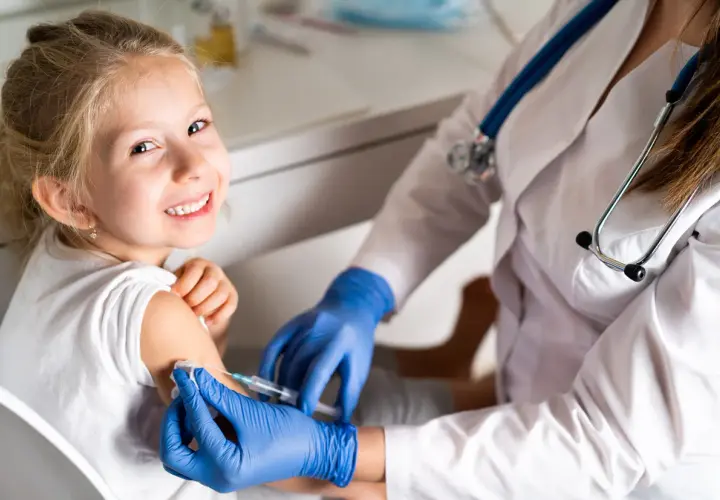 Niña sonriente recibe vacuna contra la gripe. Es recomendable vacunar a los niños de la gripe para proteger su salud.