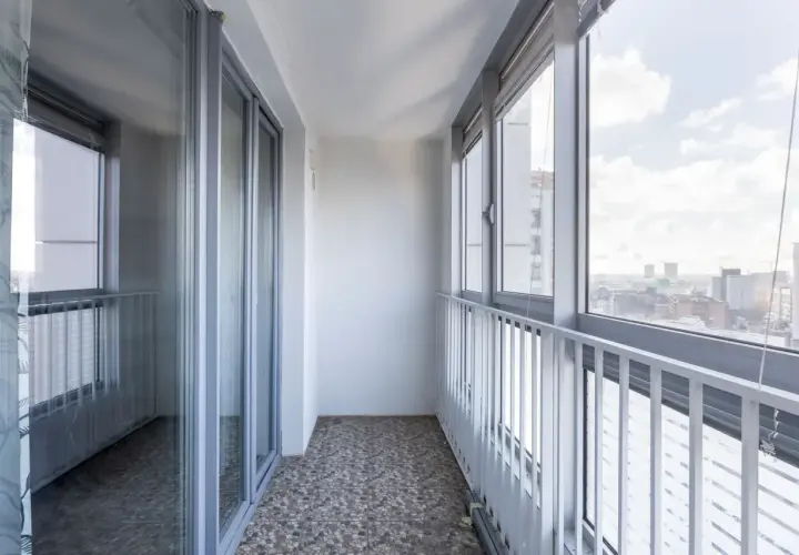 Szare okna i drzwi balkonowe, biała balustrada i widok na miasto. Idealne miejsce, by zastanowić się, czym osłonić balkon.
