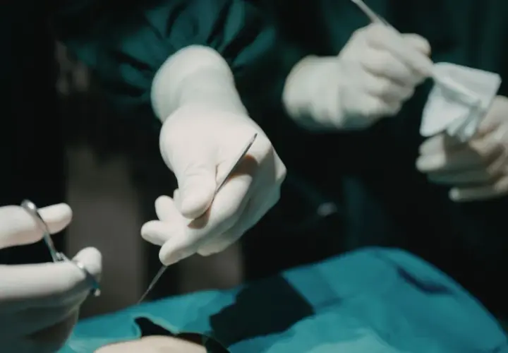 Dłonie chirurga i anestezjologa w białych rękawiczkach przygotowują narzędzia do operacji.