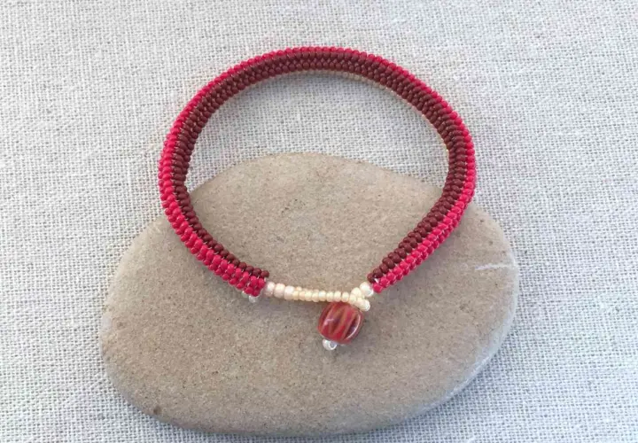 Braccialetto fatto a mano con nodi per braccialetti elastici, perline rosse e marroni, e una perlina centrale striata.