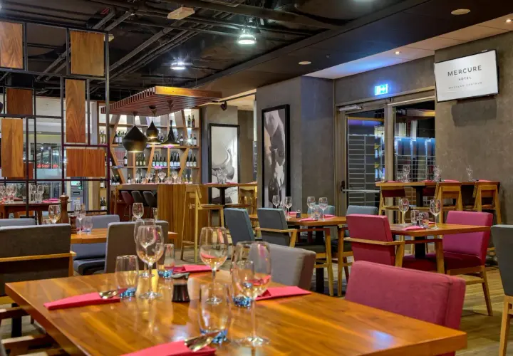 Elegancka restauracja w hotelu Mercure Wrocław Centrum. Drewniane stoły, czerwone i szare krzesła, półki z winami.