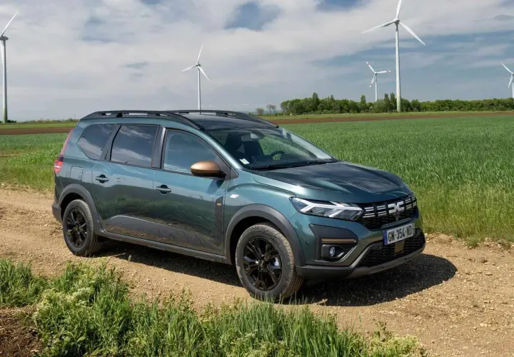 Dacia Jogger verde su sterrato, con pale eoliche sullo sfondo. Un'auto perfetta per un viaggio in autostrada con **GPL**.
