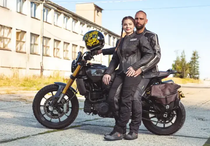 Para motocyklistów w skórzanych ubraniach siedzi na motocyklu Indian, obok stoi kask.