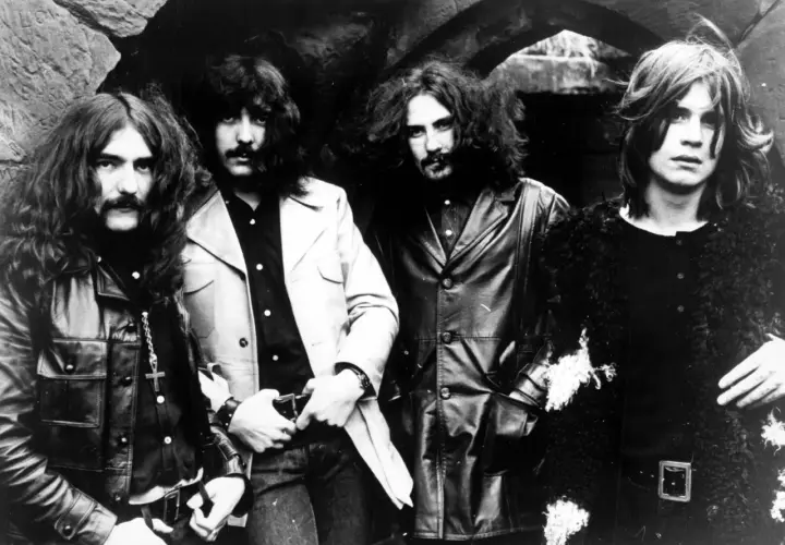 Czterech muzyków Black Sabbath, w tym wokalista, pozuje do zdjęcia w rockowych strojach.