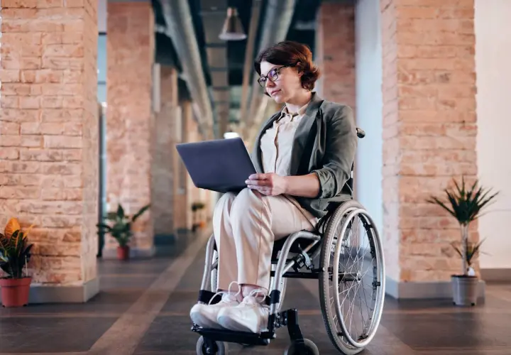 Kobieta na wózku inwalidzkim pracuje na laptopie w nowoczesnym biurze. Zlecenie na wózek inwalidzki zostało zrealizowane.