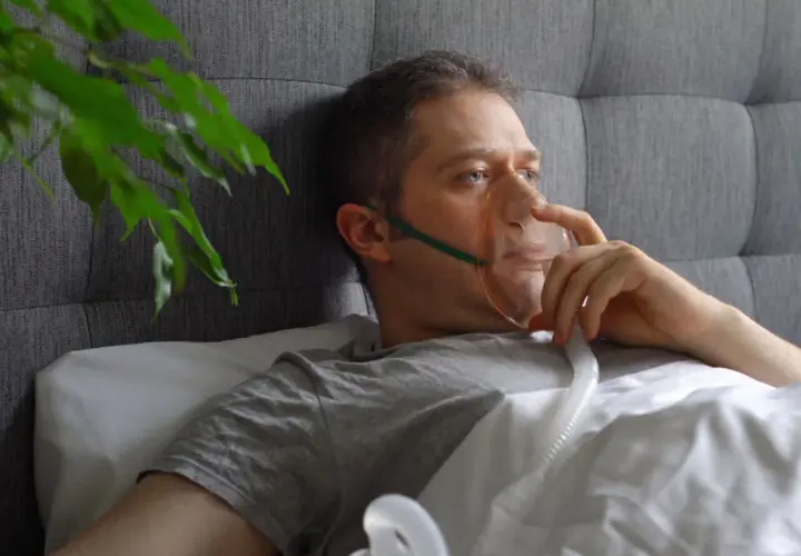 Mężczyzna w łóżku z maską tlenową, która pomaga mu oddychać. Sól fizjologiczna do inhalacji ułatwia mu powrót do zdrowia.