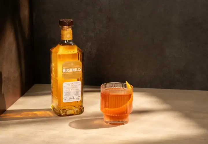 Butelka Bushmills 15 Year Old Single Malt Irish Whiskey obok szklanki z drinkiem. Wiele pozytywnych bushmills whisky opinie potwierdza jego wyjątkowy smak.