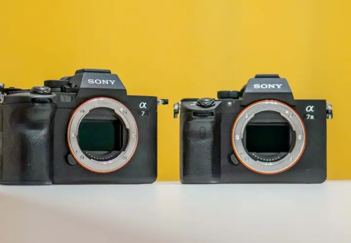 Dwa aparaty Sony Alpha, jeden z nich to sony a7 iiis, stoją obok siebie na białej powierzchni, na żółtym tle.