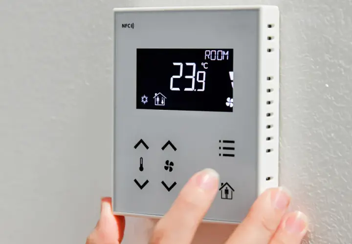 Dłoń reguluje termostat, pokazując jak ustawić temperaturę na pompie ciepła. Aktualna temperatura to 23.9°C.