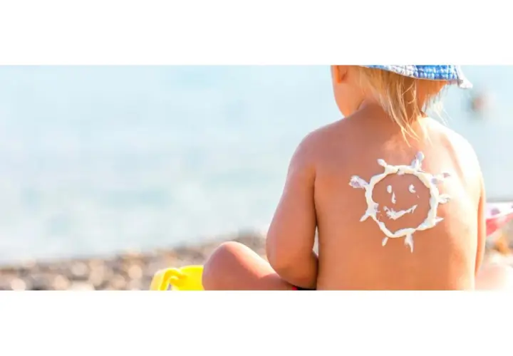 Bambino con crema solare a forma di sole sulla schiena, al mare. Protezione per la dermatite atopica e il sole.