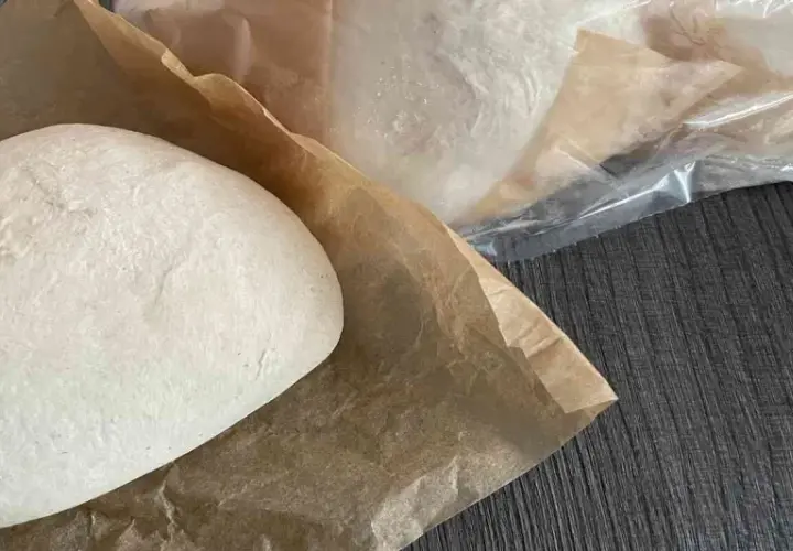 Frische Pizzaböden, bereit für das Pizzateig einfrieren. Einer liegt auf Backpapier, weitere sind in Folie verpackt.