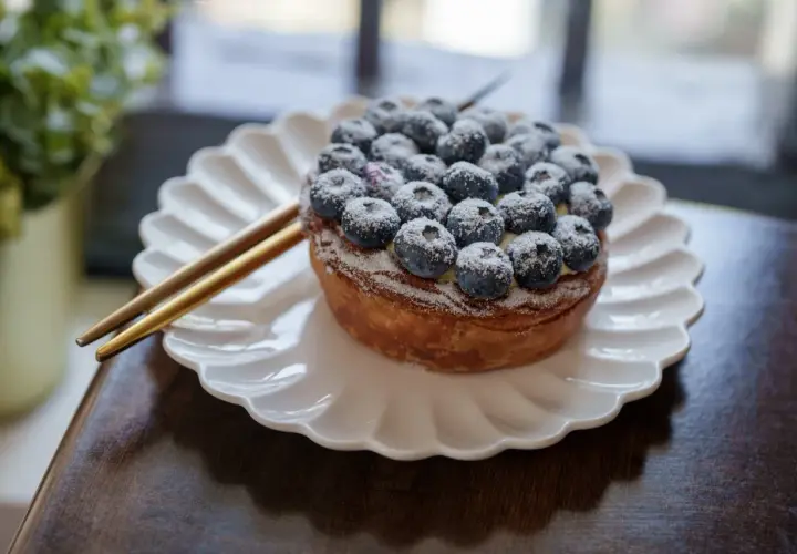 Tarte myrtille Savoie, une gourmandise aux myrtilles fraîches saupoudrée de sucre glace, servie sur une assiette blanche.