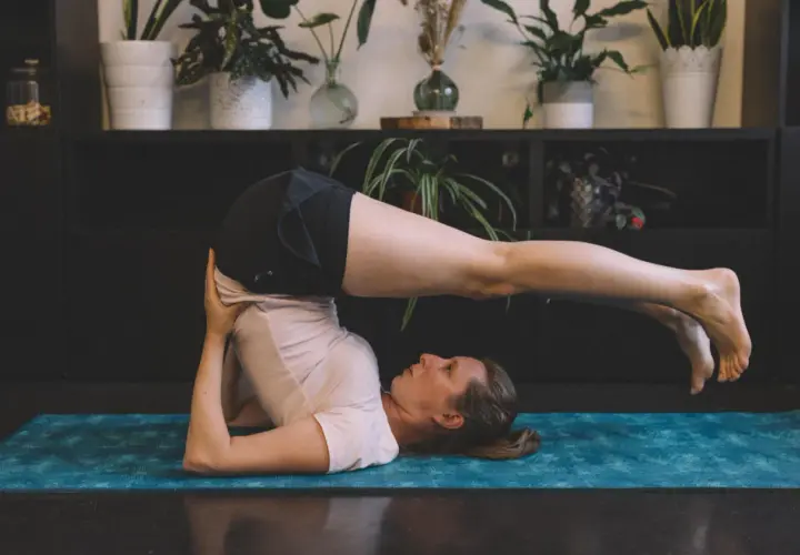 Femme effectuant des étirements du dos sur un tapis de yoga bleu. Ses jambes sont levées et tendues au-dessus de sa tête.