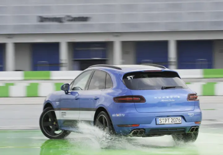Niebieski Porsche Macan Turbo na mokrym torze Driving Center, rozpryskuje wodę. DSC co to? System stabilizacji toru jazdy.