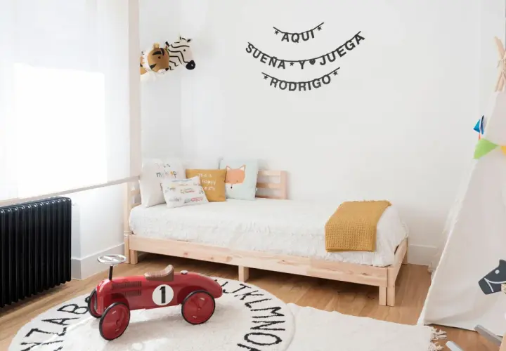 Un cuadro juego de niños con un tipi, cama, peluches y un coche de juguete rojo. "Aquí sueña y juega Rodrigo" decora la pared.