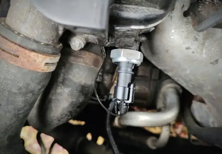 Czujnik ciśnienia oleju 2.0 TDI znajduje się w pobliżu metalowych rur i przewodów silnika.