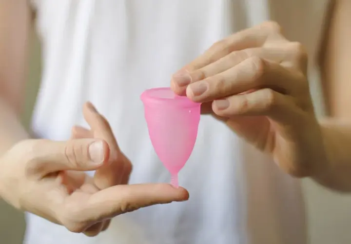Manos sostienen una copa menstrual rosa. Aprende cómo poner la copa menstrual fácilmente.