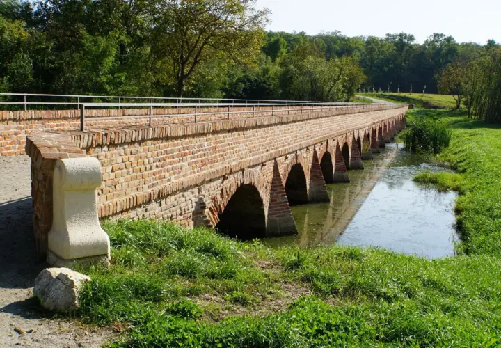 Długi, ceglany most z łukami nad wodą, idealny na trasę rowerową EuroVelo 9.