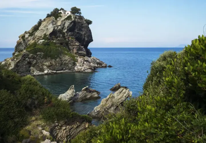 Felsige Klippe mit weißem Haus und Bäumen, umgeben von üppiger Vegetation und dem blauen Meer. Hier wurde Mamma Mia gedreht.