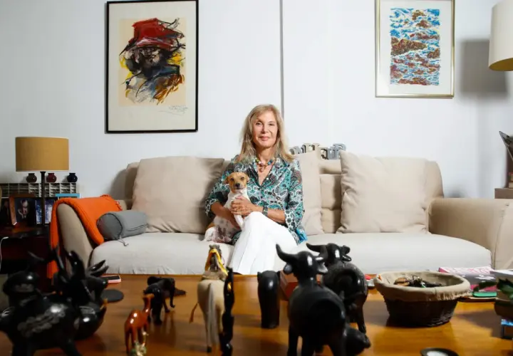Pilar Eyre, sentada en un sofá con su perro, rodeada de arte y figuras de animales. Un vistazo a su mundo para el blog.
