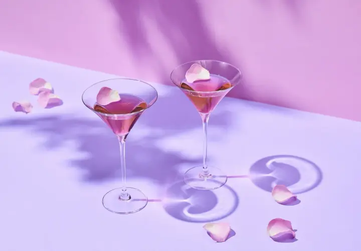 Dwa kieliszki z różowym Martini Rosso, ozdobione płatkami róż. Idealne na romantyczny wieczór. Z czym pić? Z dobrym towarzystwem!