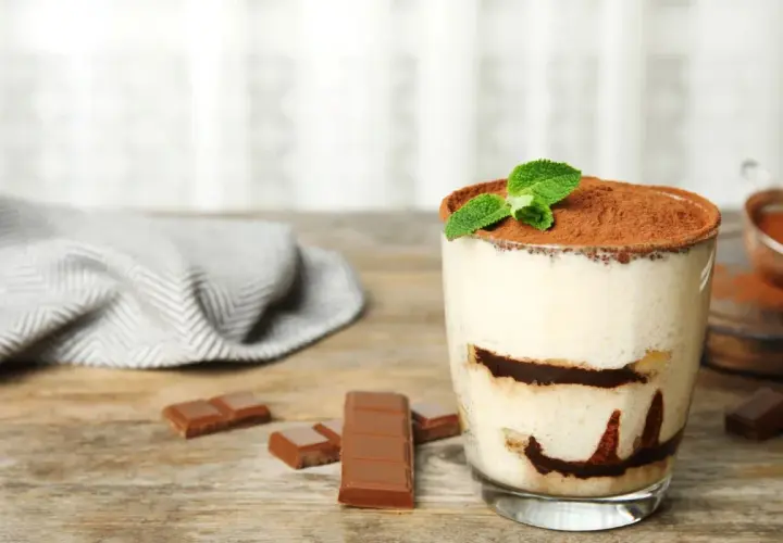 Szybki deser z niczego: kremowe tiramisu w szklance, posypane kakao i udekorowane miętą. Obok kawałki czekolady.