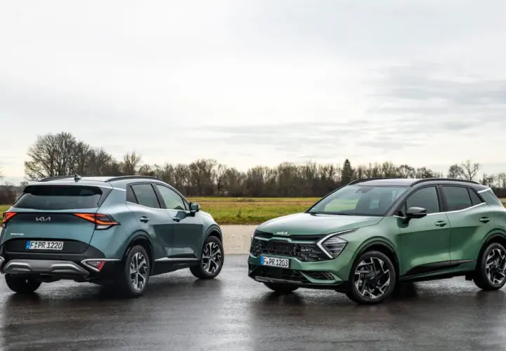 Dwa nowe Kia Sportage GT Line w zielonych odcieniach stoją na mokrej drodze.