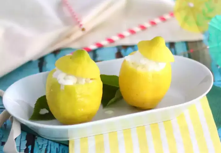 Deux citrons évidés remplis de sorbet citron, servis sur une assiette blanche, avec des feuilles vertes et des pailles colorées en arrière-plan.