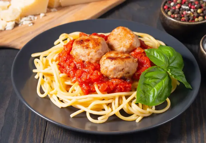 Spaghetti con tres jugosas polpette en salsa de tomate, decorado con albahaca fresca. Un plato clásico y delicioso.