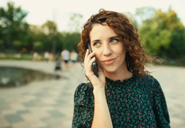 Kobieta z rudymi lokami rozmawia przez telefon, słuchając uważnie. Może właśnie zostawiła wiadomość na poczcie głosowej.