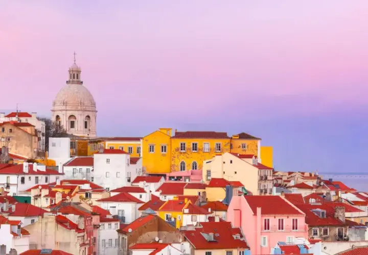 Tejado rojo y cúpula blanca bajo un cielo rosado. Un paisaje urbano que evoca las mejores experiencias en Lisboa.